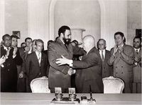 Photographie de deux hommes se serrant la main tandis que de nombreux observateurs applaudissent.